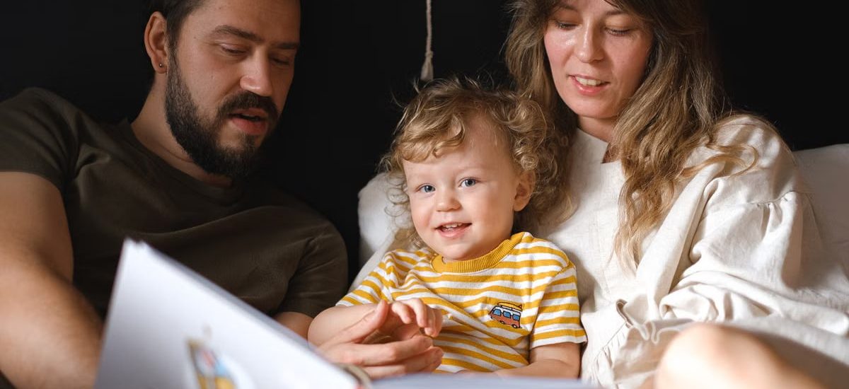 A happy family reading together, featuring parents and their smiling child enjoying a book indoors.