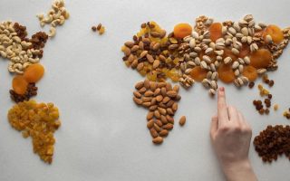 Top view of crop anonymous person making world continents with various nuts and heap of dried fruits on white background