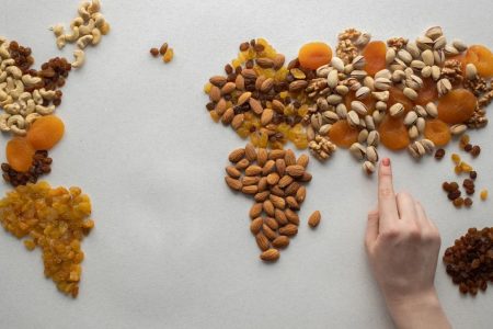 Top view of crop anonymous person making world continents with various nuts and heap of dried fruits on white background