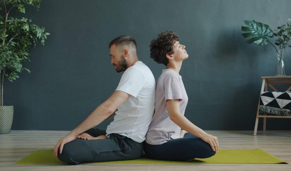 Man and woman are practising pair yoga doing warm-up exercises sitting back to back on mat in studio. Healthy lifestyle, bodycare and pairwork concept.