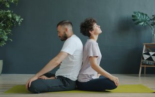 Man and woman are practising pair yoga doing warm-up exercises sitting back to back on mat in studio. Healthy lifestyle, bodycare and pairwork concept.