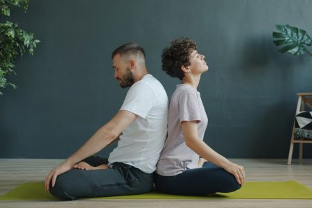 Man and woman are practising pair yoga doing warm-up exercises sitting back to back on mat in studio. Healthy lifestyle, bodycare and pairwork concept.